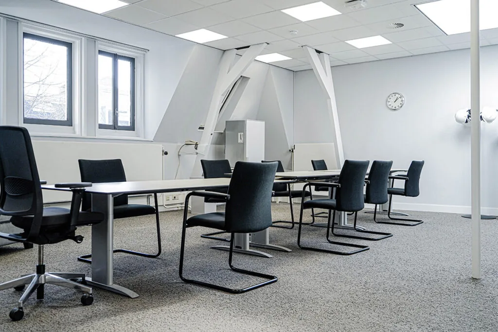 Vergaderruimte aan de Burgemeester van Karnebeeklaan met moderne inrichting en zwart-witte stoelen rond een lange tafel.
